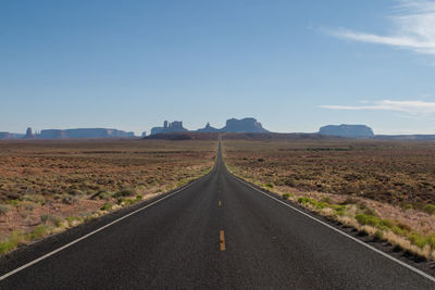 Road passing through field against clear sky