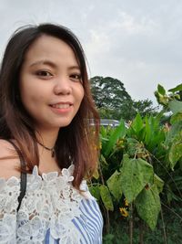 Portrait of smiling young woman by plants against sky