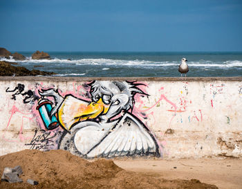 Graffiti on wall by sea against sky