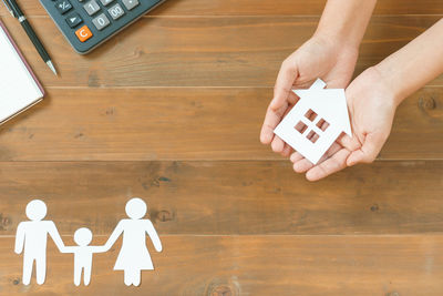 Cropped hands of business person holding paper model home over desk