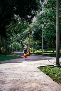 A little girl in a rainbow dress fun runs on the concrete path in the park.