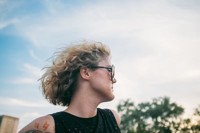 Mid adult woman wearing sunglasses while looking away against sky at sunset