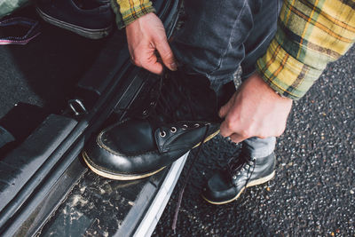 Low section of man tying shoelace while standing by car