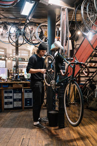 Young skilled male master repairing detail on wheel of bicycle hanging in workshop during maintenance service work