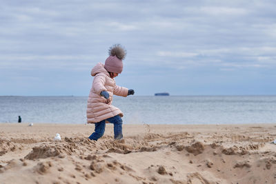 Cute girl fooling around at the beach in a winter coat