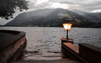 Illuminated lamp by lake against sky