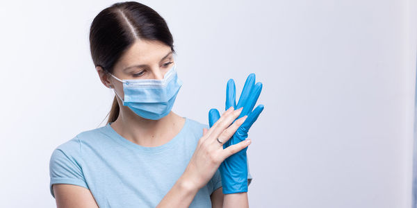 Doctor in mask wearing surgical glove against gray background