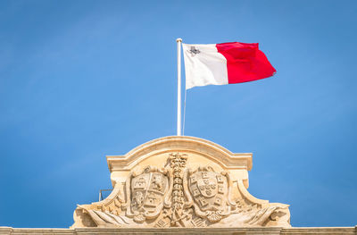 Low angle view of maltese flag on building against blue sky