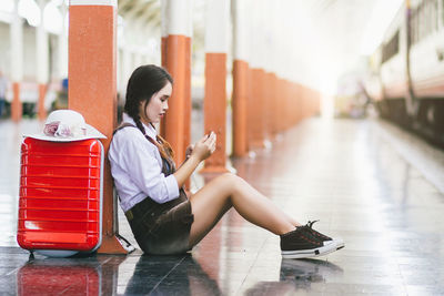 Rear view of woman using mobile phone while sitting on floor