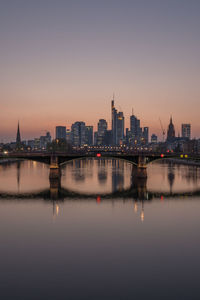Illuminated buildings by river against sky during sunset