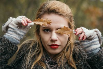 Portrait of young woman covering eye with leaf during winter