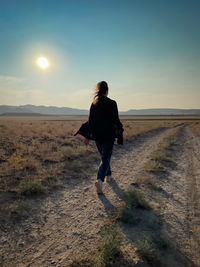 Rear view of woman walking on land during sunset