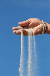 Cropped image of hand playing with sand against clear blue sky