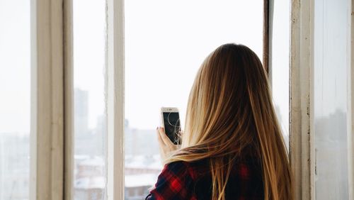 Rear view of woman using mobile phone against window