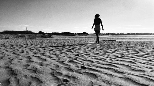 Rear view of woman walking on beach against sky