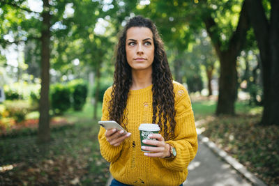 Portrait of young woman using phone while standing on tree