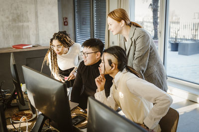 Multiracial male and female programmers discussing over computer in creative office