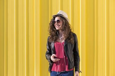 Portrait of a smiling young woman standing against yellow wall