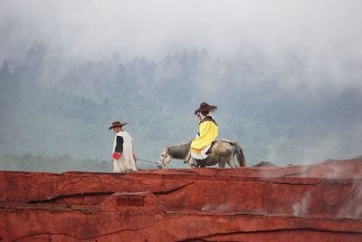Men riding horse on mountain against sky