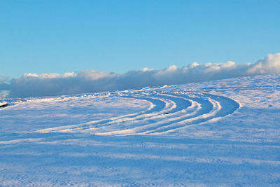 Scenic view of tracks in snow covered land against blue sky