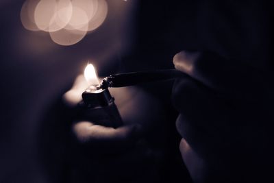 Cropped hands of person igniting cigarette in darkroom