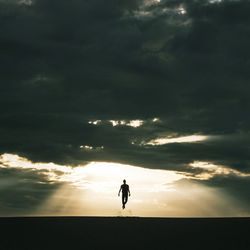 Silhouette of people on landscape against cloudy sky