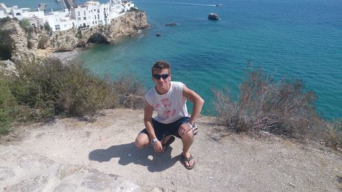 Full length portrait of man crouching against sea