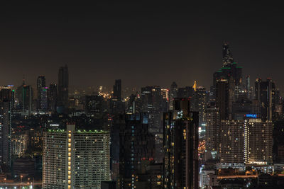 Illuminated modern buildings in city against sky at night