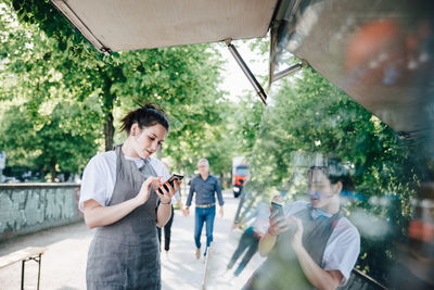 Female young owner using smart phone while standing by food truck