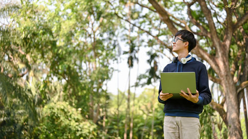 Side view of man using digital tablet while standing against trees