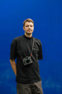 Young man with camera standing against blue background