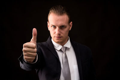 Portrait of confident businessman gesturing thumbs up against black background