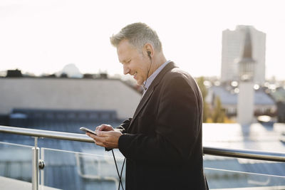 Mature businessman listening music through phone while standing at office