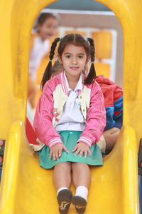 Portrait of cute smiling girl sitting on slide at playground
