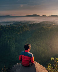 Rear view of man looking at mountains while sitting on rock