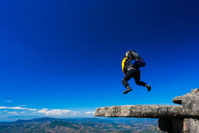 Man jumping on rock against blue sky