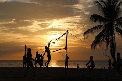 Silhouette people playing volleyball at beach against cloudy sky during sunset