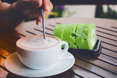 Cropped hand of person stirring coffee in cup on table at cafe