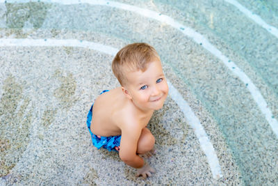 High angle portrait of cute boy crouching in pool