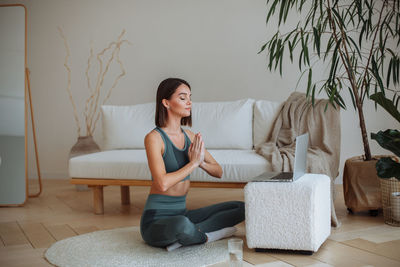 A young woman practices yoga at home in a tracksuit. sitting in the lotus position