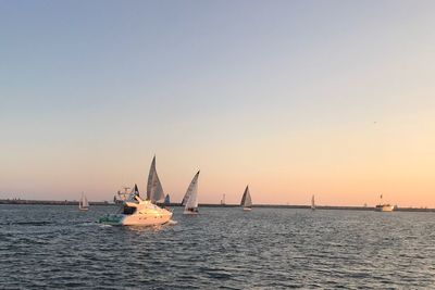 Sailboats sailing on sea against clear sky during sunset