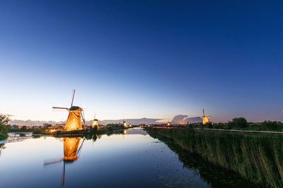 Traditional windmill by lake against blue sky