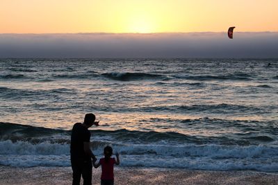 Rear view of father and daughter standing on shore during sunset