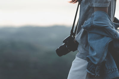 Midsection of man holding mobile phone against sky