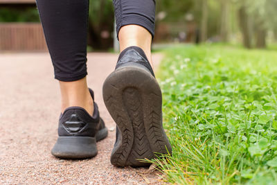 A womans legs, in black sneakers , walking along a path made of small red stone