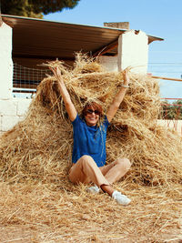 Young woman sitting near haystack with hands up