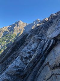 Low angle view of rocky mountains against clear blue sky