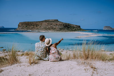 Rear view of woman sitting on beach against sky