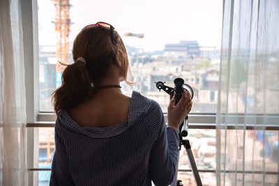 Rear view of woman standing by telescope at home