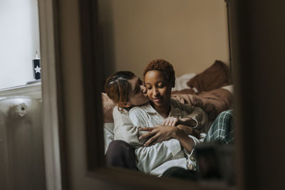 Non-binary person kissing friend while sitting in bedroom at home